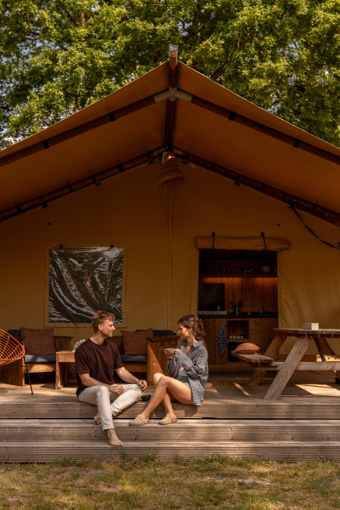 Una coppia seduta sulla veranda di una tenda safari a De Bos Escape, Gooise Heide, Paesi Bassi, che conversa.