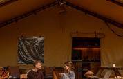 Ein Paar sitzt auf der Veranda eines Safarizeltes bei De Bos Escape, Gooise Heide, Niederlande, und plaudert.