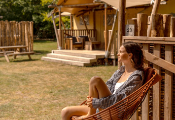 Kvinde slapper af på verandaen ved safari-teltet De Bos Escape på Gooise Heide i Holland, solrig dag.