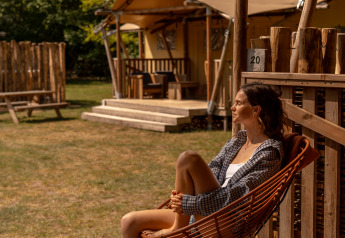 Femme détendue devant la tente safari De Bos Escape à Gooise Heide, Pays-Bas, journée ensoleillée.