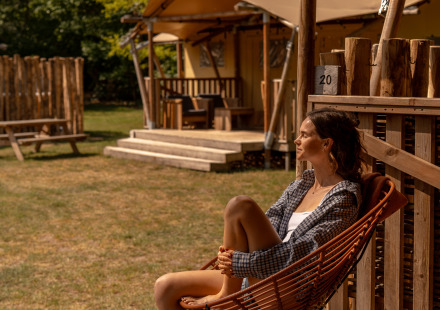 Vrouw ontspant op de veranda bij safaritent De Bos Escape op de Gooise Heide, Nederland, zonnige dag.