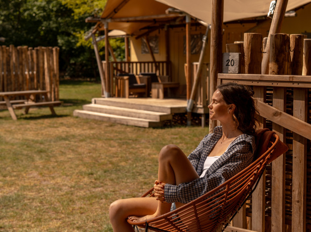 Vrouw ontspant op de veranda bij safaritent De Bos Escape op de Gooise Heide, Nederland, zonnige dag.