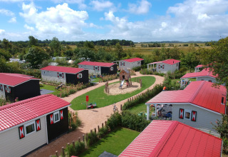 Luchtfoto van vakantiehuisjes met rode daken en speeltuin bij Camping Ginsterveld, Zeeland, Nederland.
