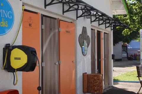 Baños exteriores de glamping con puertas naranjas para WC y familia y enrollador de manguera al lado.