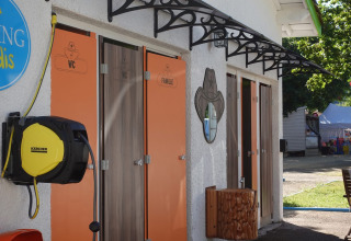 Baños exteriores de glamping con puertas naranjas para WC y familia y enrollador de manguera al lado.