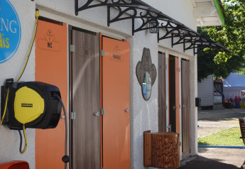 Baños exteriores de glamping con puertas naranjas para WC y familia y enrollador de manguera al lado.