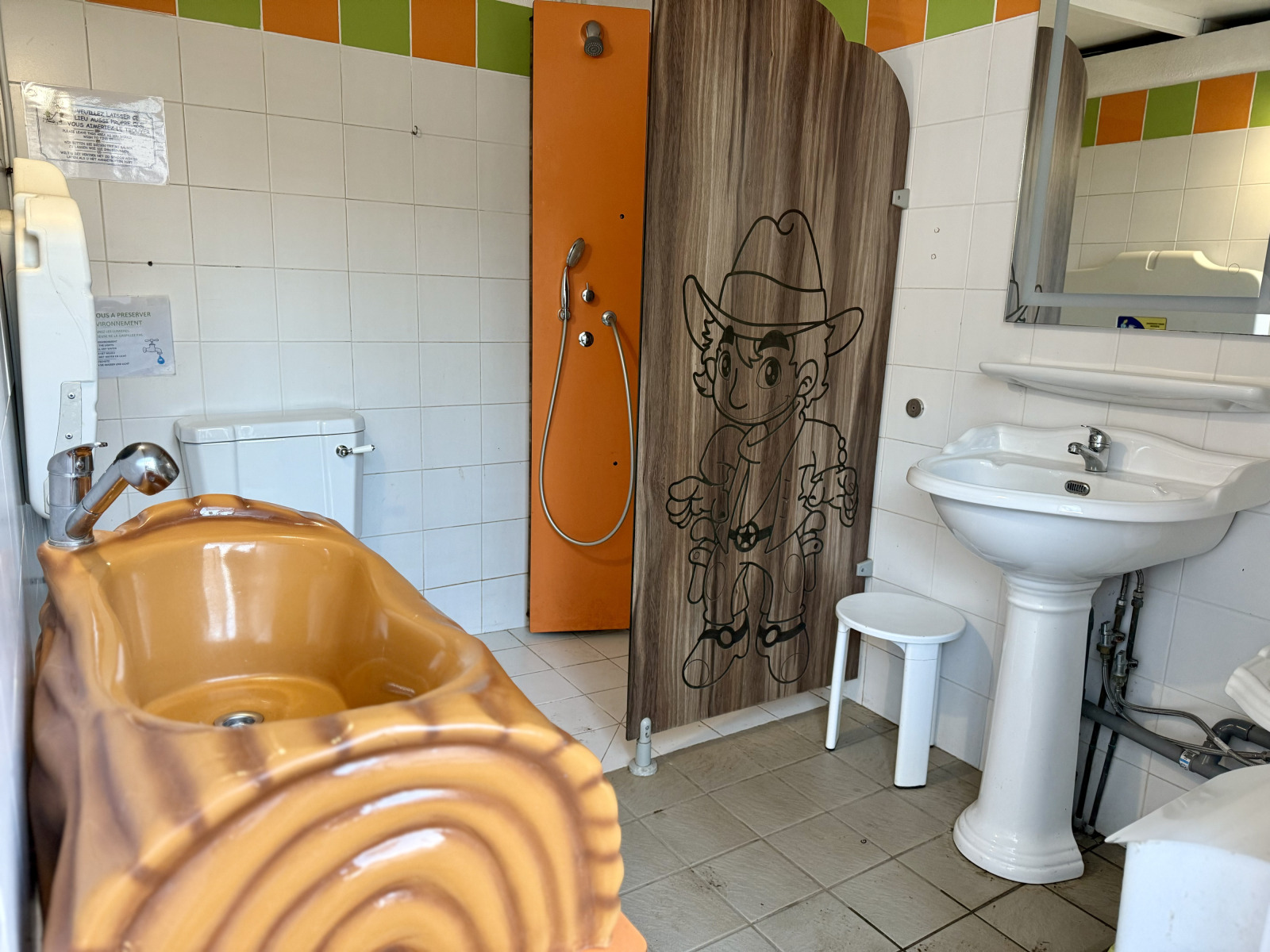 Glampingbadkamer met bruine badkuip, douche met cowboytekening, toilet en wastafel onder spiegel.