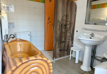 Baño de glamping con bañera marrón, ducha con dibujo de vaquero, inodoro y lavabo bajo espejo.