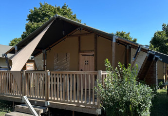 Tenda safari chiamata Villatent Outback con veranda in legno, verde attorno e cielo azzurro.