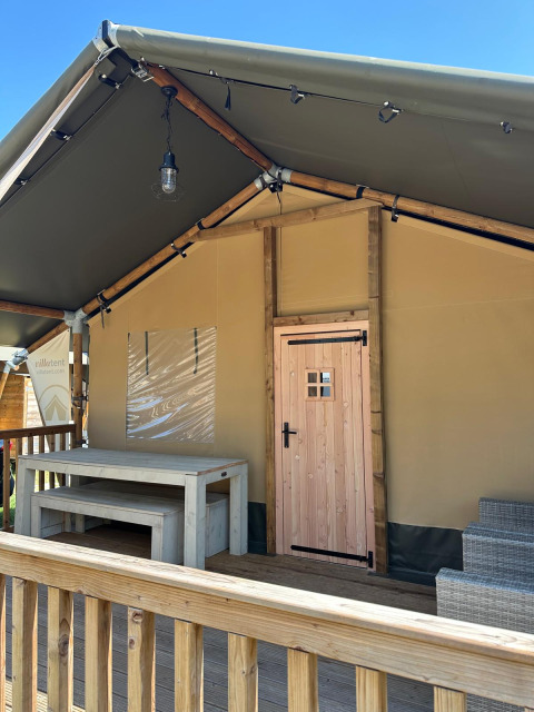 Vista della veranda di una tenda safari con tavolo e panche in legno al Villatent Outback sotto cielo blu.