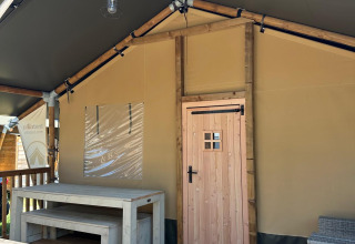 View of a safari tent porch with wooden table and benches at Villatent Outback under a blue sky.
