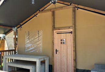 Vista della veranda di una tenda safari con tavolo e panche in legno al Villatent Outback sotto cielo blu.