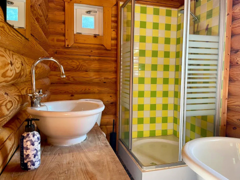 Bagno rustico in una baita con pareti in legno, lavabo bianco e doccia con piastrelle verdi e gialle.