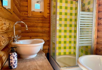 Bagno rustico in una baita con pareti in legno, lavabo bianco e doccia con piastrelle verdi e gialle.