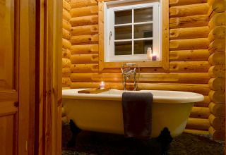 Bagno accogliente in un lodge di tronchi con vasca indipendente, candele e finestrella sopra.
