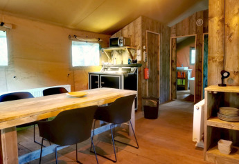 Interieur van een glamping safaritent met houten tafel en keuken bij Outdoors Holten, Nederland.