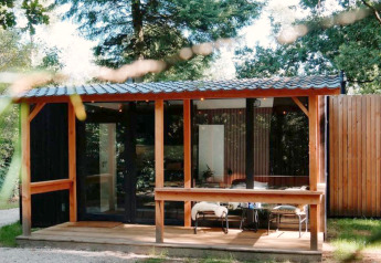 Cabane forestière avec terrasse chez Outdoors Holten aux Pays-Bas, entourée d’arbres et clôture bois.