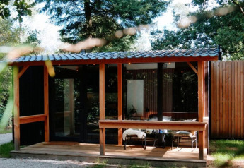 Bosrijke blokhut met houten veranda bij Outdoors Holten, Nederland, omringd door groen en bomen.