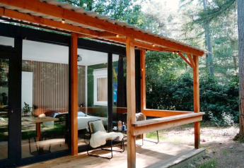 Wooden cabin with covered porch set in a forest at Forest Cabin, Outdoors Holten, Netherlands.
