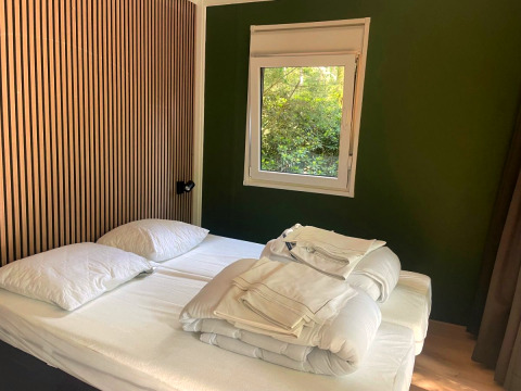 Bedroom in Forest Cabin at Outdoors Holten, Netherlands, with twin beds, green wall, and window view.