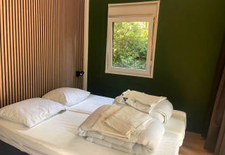 Bedroom in Forest Cabin at Outdoors Holten, Netherlands, with twin beds, green wall, and window view.
