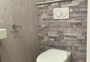 Modern toilet in Forest Cabin bij Outdoors Holten, Nederland, met wandtoilet en grijze steenmuur.