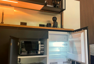 Modern kitchenette inside Forest Cabin at Outdoors Holten, Netherlands, with open mini fridge and microwave.