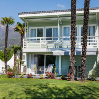 Modern chalet with balcony and palm trees at Campofelice Village Camping at Lake Maggiore, Switzerland.