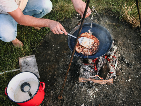 Persona cocinando panqueques en una fogata en un parque vacacional en Overijssel, Países Bajos, junto a una olla roja.
