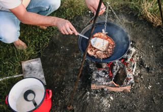 Persona cocinando panqueques en una fogata en un parque vacacional en Overijssel, Países Bajos, junto a una olla roja.