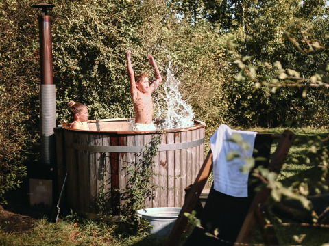 Dos niños disfrutan de una bañera de hidromasaje al aire libre en BoerenBed De Kalverweide, Países Bajos, rodeados de naturaleza.