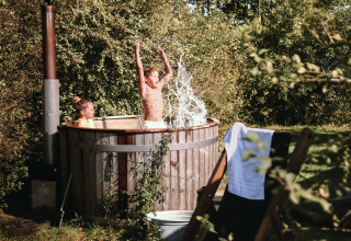 Dos niños disfrutan de una bañera de hidromasaje al aire libre en BoerenBed De Kalverweide, Países Bajos, rodeados de naturaleza.
