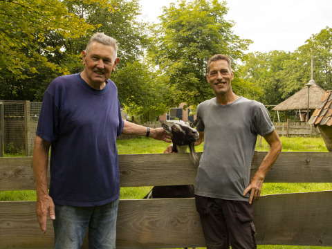 Dos hombres y una cabra posan junto a una valla de madera en BoerenBed Het Boshuis, Gelderland, Países Bajos.