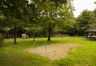 Kleines Fußballfeld mit Toren und Holzhütten in einem grünen Ferienpark bei BoerenBed Het Boshuis, Gelderland.