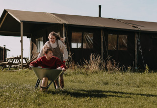 Deux enfants jouent avec une brouette devant une tente à BoerenBed Hoeve den Overdraght, Flandre-Occidentale, Belgique.