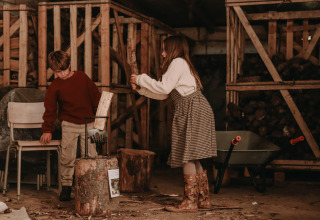 Zwei Kinder hacken gemeinsam Holz in einer Scheune im Ferienpark BoerenBed Hoeve den Overdraght, Belgien.
