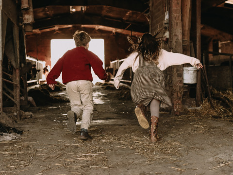 Deux enfants courent joyeusement dans une grange à BoerenBed Hoeve den Overdraght, parc de vacances en Flandre-Occidentale.