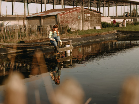 A child sits by the pond at BoerenBed Hoeve den Overdraght, a holiday park in West Flanders, Belgium.