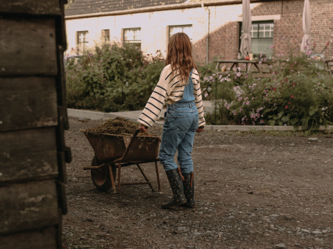 Een kind met laarzen en overall duwt een kruiwagen met hooi bij BoerenBed Hoeve den Overdraght.