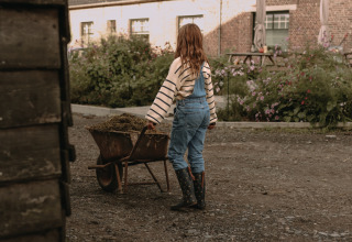 Un niño con botas y peto lleva una carretilla con heno en BoerenBed Hoeve den Overdraght, Bélgica.