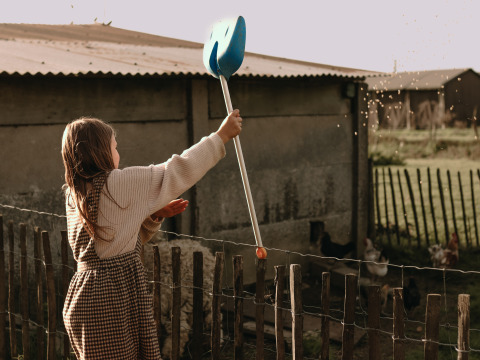 A child feeds chickens with a blue scoop at BoerenBed Hoeve den Overdraght holiday park in West Flanders, Belgium.