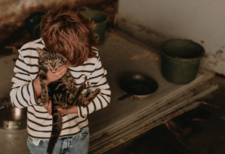 Child in striped sweater lovingly holding a cat at BoerenBed Hoeve den Overdraght holiday park in Belgium.