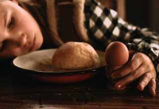 Ein Kind lehnt den Kopf auf den Tisch neben einem Brötchen und einem Ei in Westflandern, Belgien.