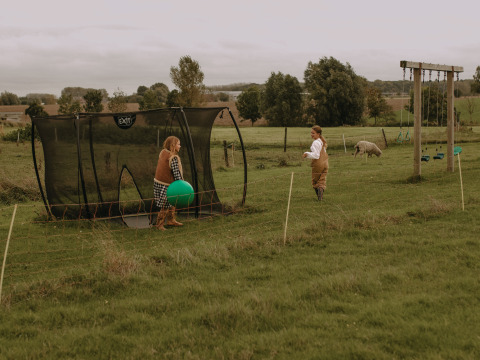 Zwei Kinder spielen mit einem Ball und Trampolin auf einer Wiese mit Schafen bei BoerenBed Hoeve den Overdraght.