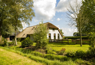 Ferme au toit de chaume entourée de verdure à BoerenBed De Lange Weide, parc de vacances à Drenthe, Pays-Bas.