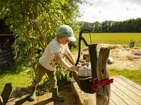 Et barn pumper vand ved en gammel vandpumpe på en legeplads i landlige Drenthe, Holland, solskinsdag.
