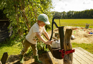 Un enfant actionne une vieille pompe à eau sur une aire de jeux ensoleillée à Drenthe, Pays-Bas.