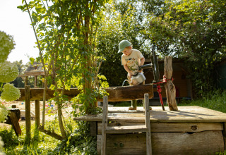 Un enfant en casquette remplit une bouilloire à une pompe à eau dans le jardin ensoleillé de BoerenBed De Lange Weide, Drenthe.