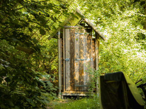 Wooden outhouse surrounded by lush greenery at BoerenBed De Lange Weide holiday park in Drenthe, Netherlands.
