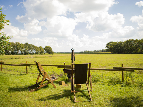 Twee stoelen uitkijkend over een groen veld met bomen bij BoerenBed De Lange Weide, vakantiedorp Drenthe.